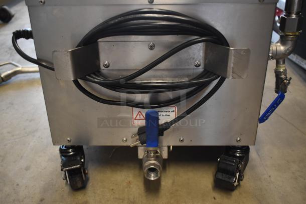 Industrial stainless steel machine with cord holder, warning label for oil evacuation, mounted on casters.