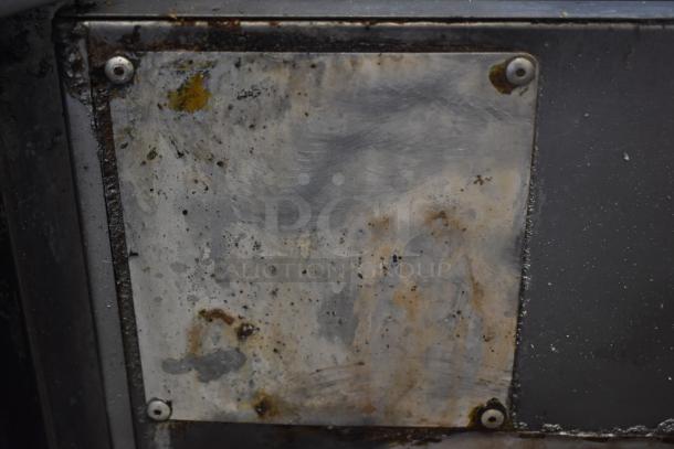 Rusty, metal plate with visible corrosion and wear. Four screws at corners, suggesting attachment. No visible markings or labels.