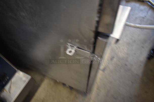 Blurry image of a metal cabinet or equipment with a latch handle, situated on a floor with visible cables. Condition unclear.