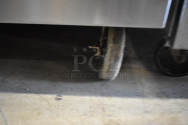 Blurred metal cart or equipment with visible wheel on concrete floor. Signs of wear and use. No visible tags or markings.