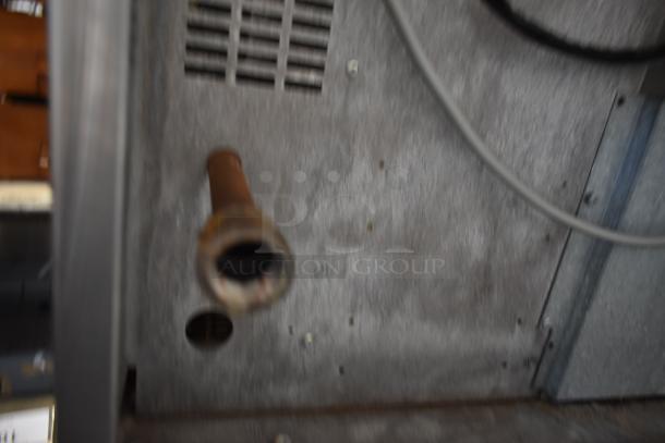Close-up of a metal appliance interior with a protruding copper pipe, vent holes, and wiring. Industrial condition.