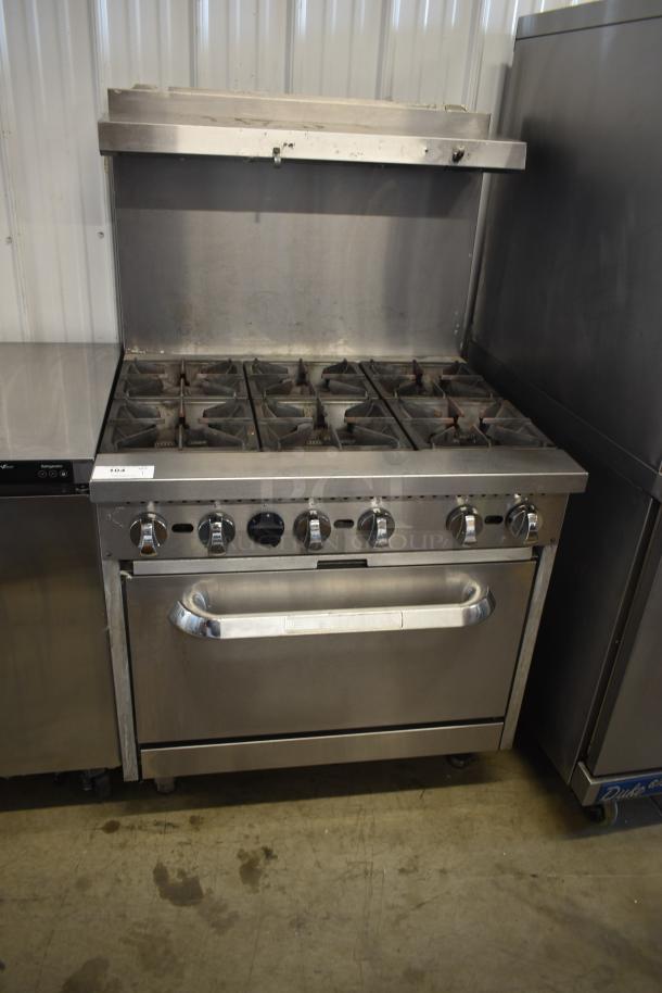 Commercial stainless steel gas range with six burners and oven, used condition, control knobs intact, labeled '104'.