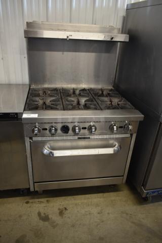 Commercial stainless steel gas range with six burners and oven, used condition, control knobs intact, labeled '104'.