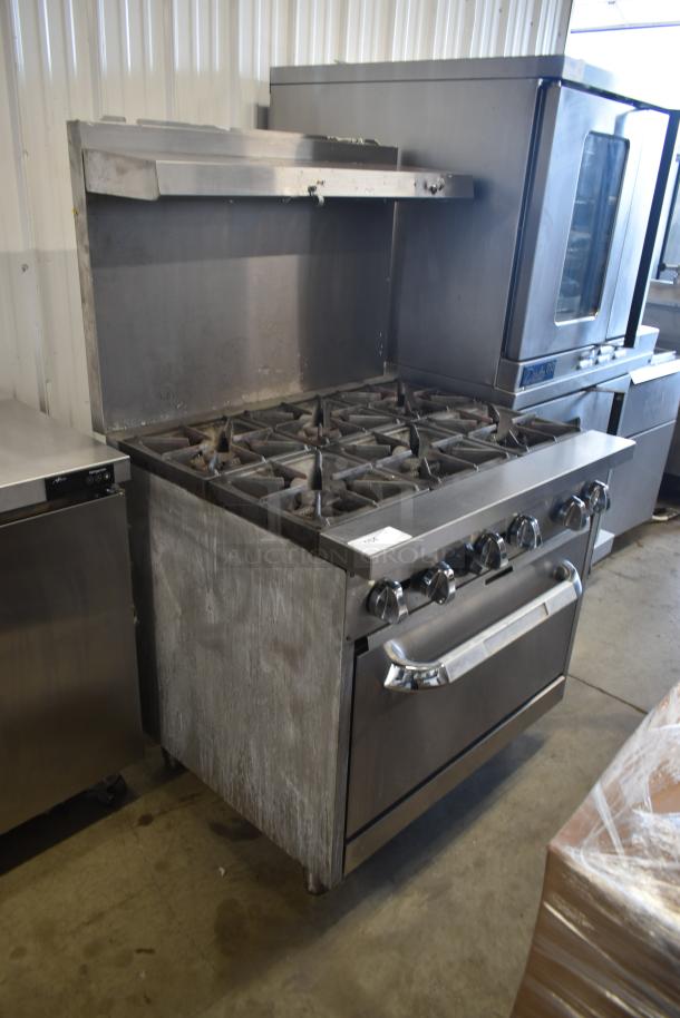 Commercial gas range with six burners, stainless steel, used condition, includes oven below. Tag reads "PCB."