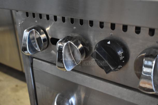 Stainless steel stove with chrome and black control knobs, showing temperature settings. Slight wear on surface.