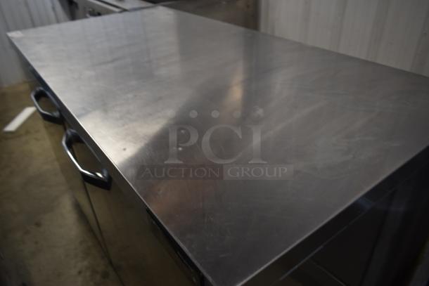Stainless steel commercial kitchen worktable with storage, handles, and minimalist design. Slight surface wear noted.