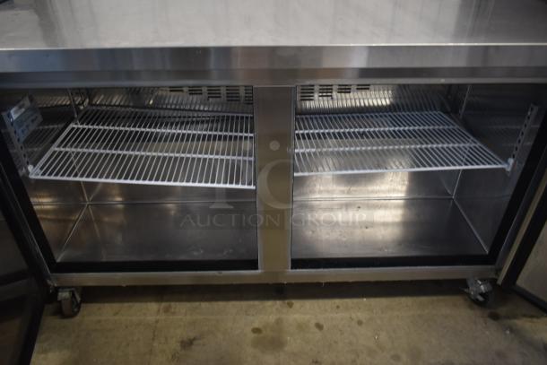 Stainless steel commercial refrigerator with double sliding doors and wire shelving, in good condition, on caster wheels.
