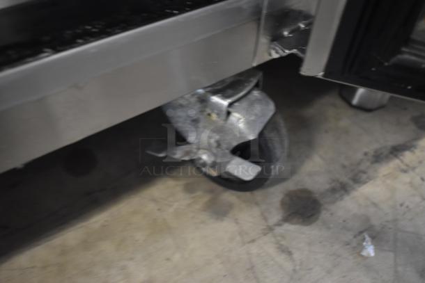 Close-up of a metal caster wheel on industrial equipment, showing moderate wear. Visible brake lever for locking.