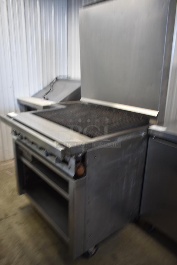 Commercial stainless steel grill with shelf space, showing signs of use. Ideal for restaurant kitchens, on wheels for mobility.
