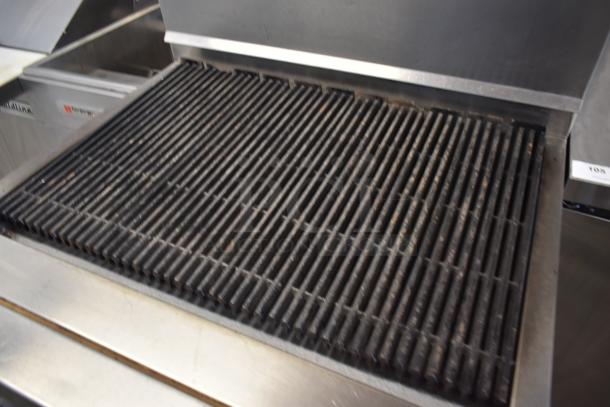 Commercial gas grill with cast iron grates, stainless steel frame; shows signs of use, model label partially visible.