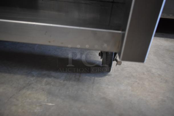 Stainless steel cart with wheels, slightly worn, on concrete floor. Durable structure, ideal for industrial use.