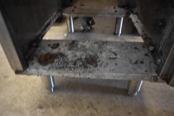 Metal shelving unit, heavily used with visible rust and wear, supported on steel legs. Ideal for industrial use.