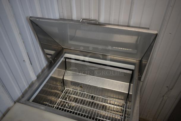 Stainless steel commercial freezer with open lid, showing metal interior and wire shelf. Clean and well-maintained condition.