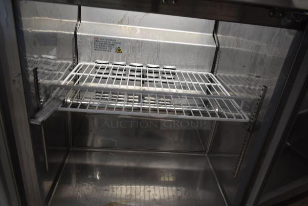 Stainless steel commercial refrigerator interior with wire shelf, warning labels, and minor wear visible.