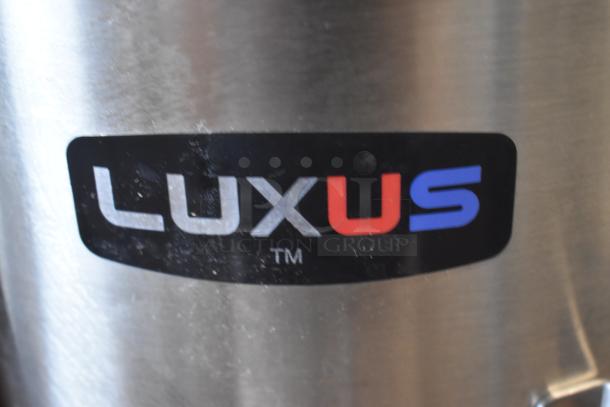 Stainless steel container with "LUXUS" logo in black, red, and blue. Surface shows minor wear.