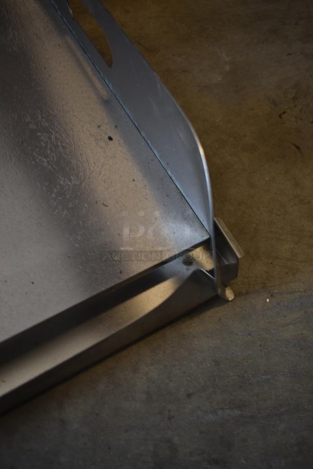 Close-up of a metal sheet with bent edge and cut-out handle, showing slight wear and surface markings.