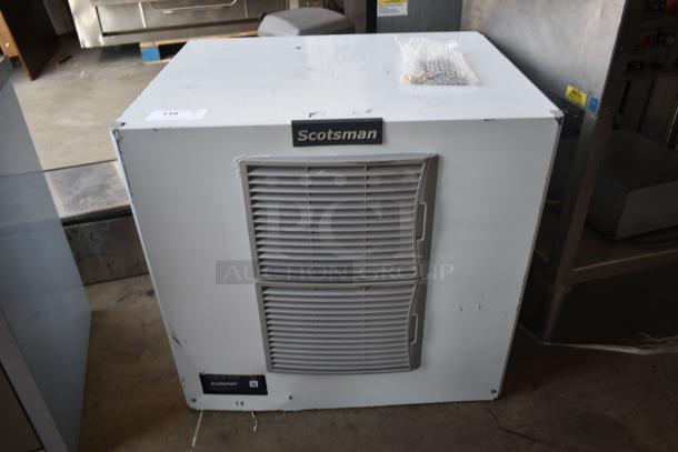Scotsman ice machine with front vents, showing some wear. Includes manufacturer label and unidentified item in bubble wrap on top.