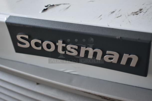 Scotsman ice machine with visible scratches and wear, metallic brand logo on exterior panel, indicates prior use.
