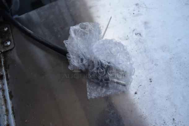 Plug wrapped in bubble wrap on a metallic surface, showing minimal wear. Power cable attached, no visible markings.