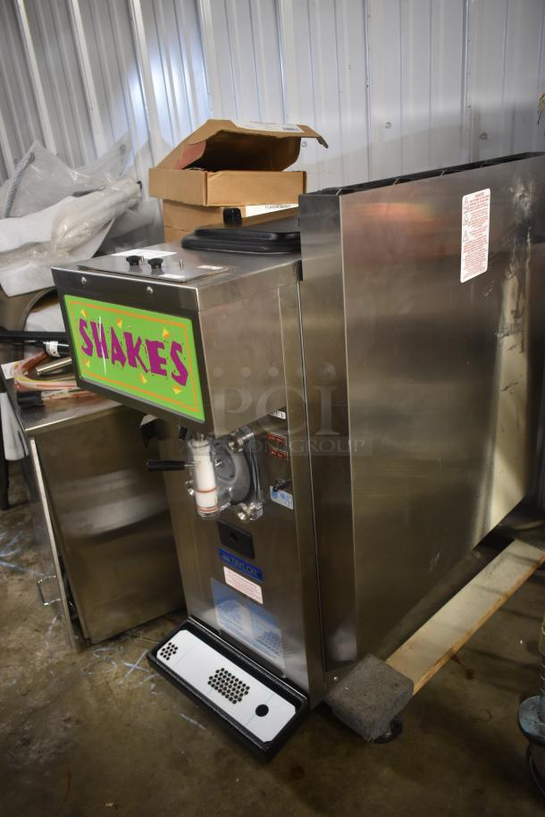 Commercial shake machine by Taylor, stainless steel, with "SHAKES" sign. Includes operational labels. Appears in good condition.