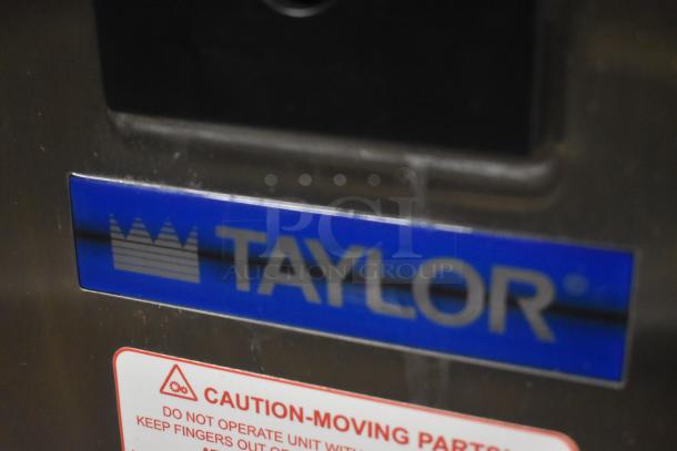 Close-up of a Taylor machine with a visible blue logo and a caution label about moving parts.