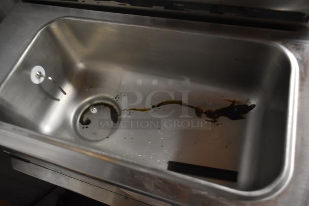 Stainless steel sink with drain, showing signs of wear and residue. No visible labels or markings. Suitable for kitchen use.