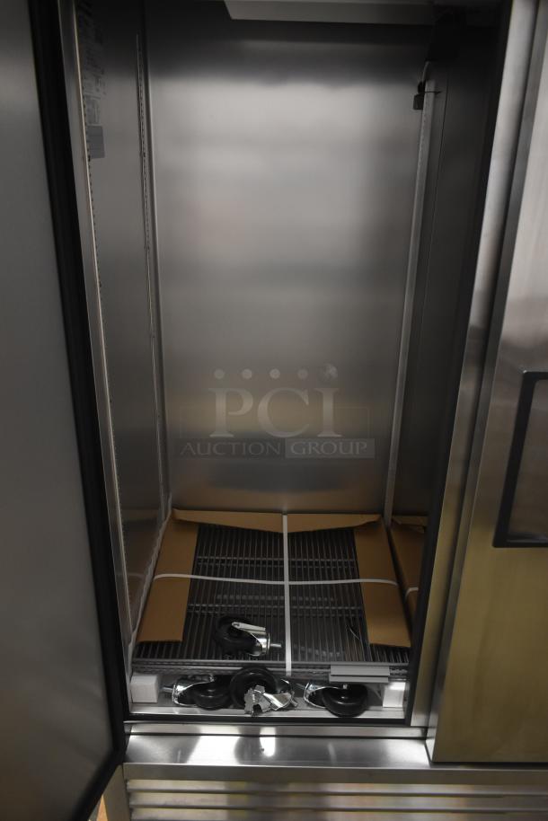 Commercial stainless steel refrigerator interior, new condition, includes shelving and caster wheels for mobility.