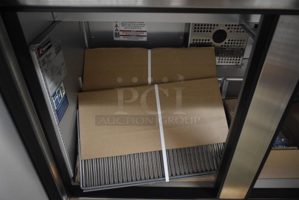 Industrial refrigerator interior with cardboard and metal shelving. Labels indicate brand "True" and model specifics.
