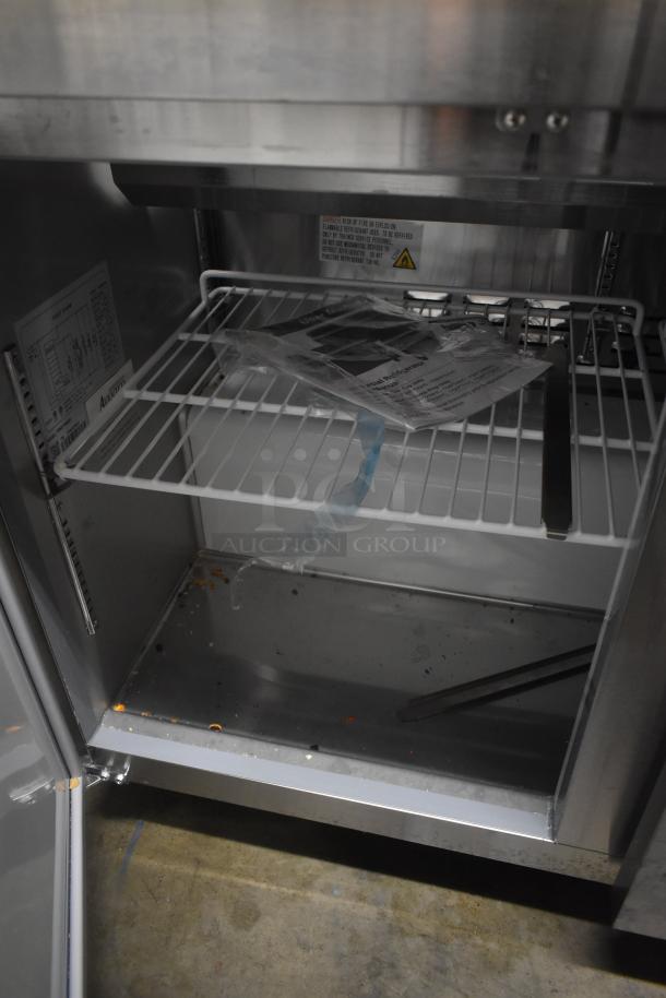 Commercial stainless steel refrigerator interior with wire shelf. Visible instructions and safety labels. Condition: used.