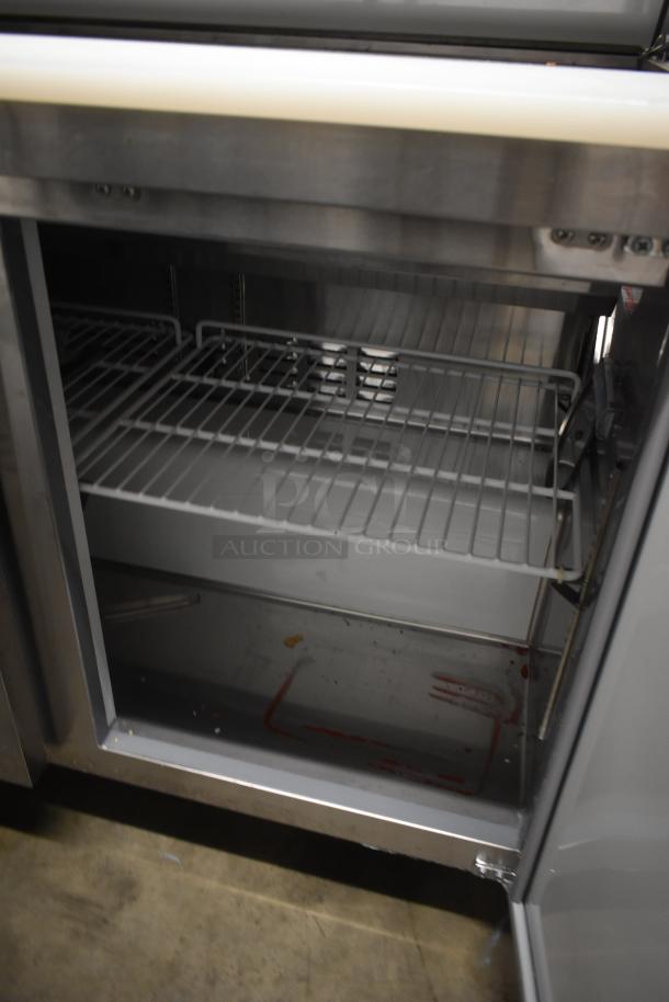 Commercial stainless steel refrigerator interior, two wire shelves, showing wear, minor stains on floor, used condition.
