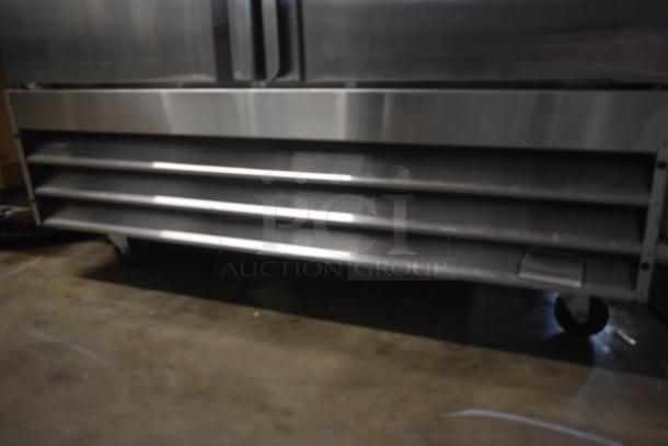 Commercial stainless steel refrigerator base with vented front panel and wheels, in used condition.