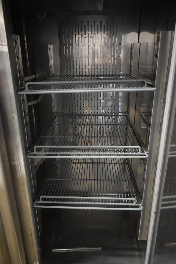 Commercial stainless steel refrigerator interior with three wire shelves, in good condition, featuring a perforated back panel for ventilation.