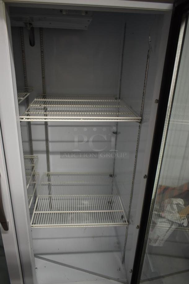 Industrial glass-door refrigerator with adjustable wire shelves. Clean interior, minor wear on surfaces. No visible tags.
