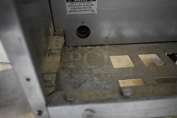 Industrial metal appliance base, partially rusted. Warning label indicates electrical shock risk and installation instructions.
