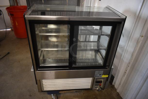 Glass display refrigerator with two sliding doors, stainless steel frame, three perforated shelves, and visible control panel in good condition.