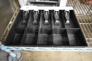 Black cash register drawer with six compartments and metal clips. Shows organizational slots for bills and coins, minor wear.