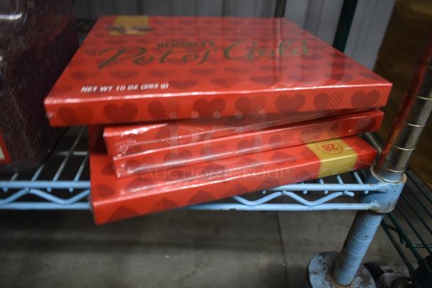 Stack of Hershey's Pot of Gold chocolate boxes, 10 oz each, sealed in red heart-patterned packaging, on a metal shelf.