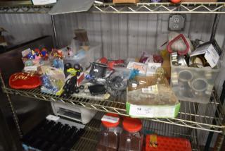 Mixed lot of household items on a metal shelf, including toys, jars, a light bulb, and various small gadgets in assorted conditions.