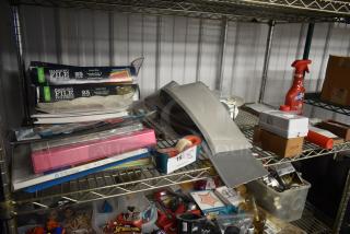 Metal shelf with assorted office supplies, hanging file folders, Scotch tape dispenser, cleaning spray, and miscellaneous items.