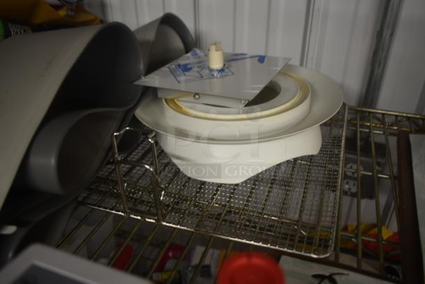 White plastic and metal ceiling fan component on wire shelf, includes blade mount and motor housing. Slight rust visible.