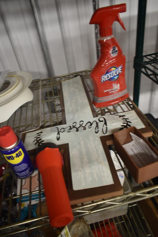 Decorative wooden cross with "Blessed" text, vintage finish, on metal shelf next to Resolve cleaner, WD-40, and red flashlight.