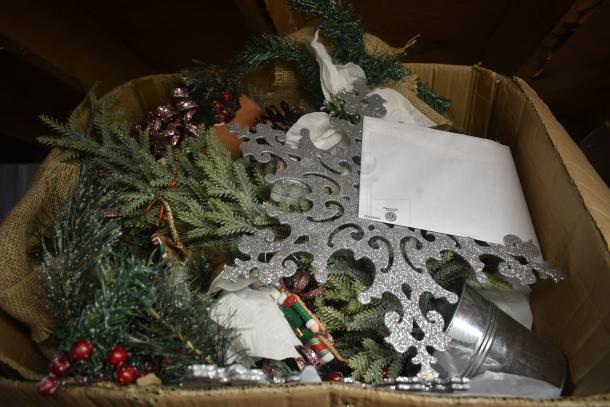 Cardboard box with assorted Christmas decorations, including a glittery silver snowflake, foliage, and a small metal bucket.