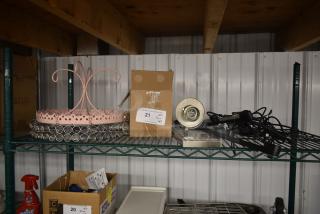 Pink metal crown-shaped stand and crystal ring display on a shelf, alongside a boxed lamp fixture, electrical cords, and a label reading "21 Qty Tier Lot." Items are in fair condition, suited for home decor or repair use.