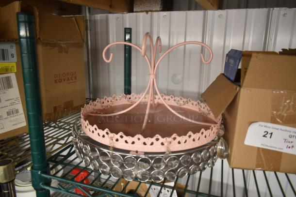 Pink metal cake stand with decorative curly top, scalloped edge, and acrylic crystal accents. Slightly worn condition.