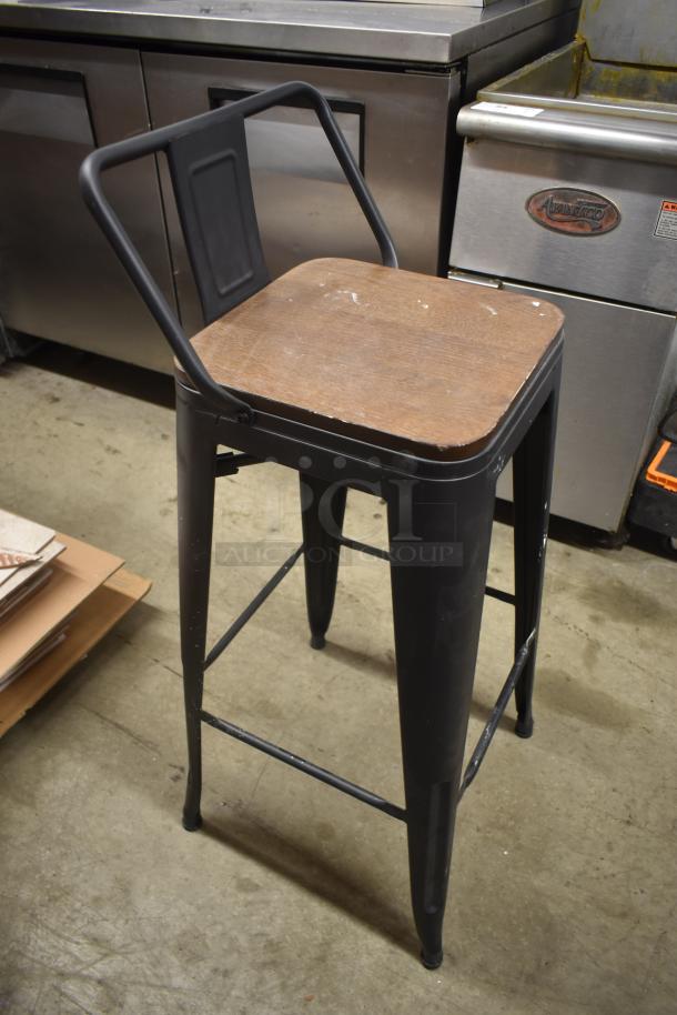 Vintage industrial-style metal bar stool with wooden seat, black finish, minor wear; ideal for rustic decor.