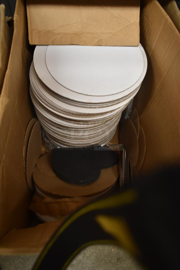 Stacked cardboard circles in a box, various sizes, mostly white with some plain brown. Appears unused.