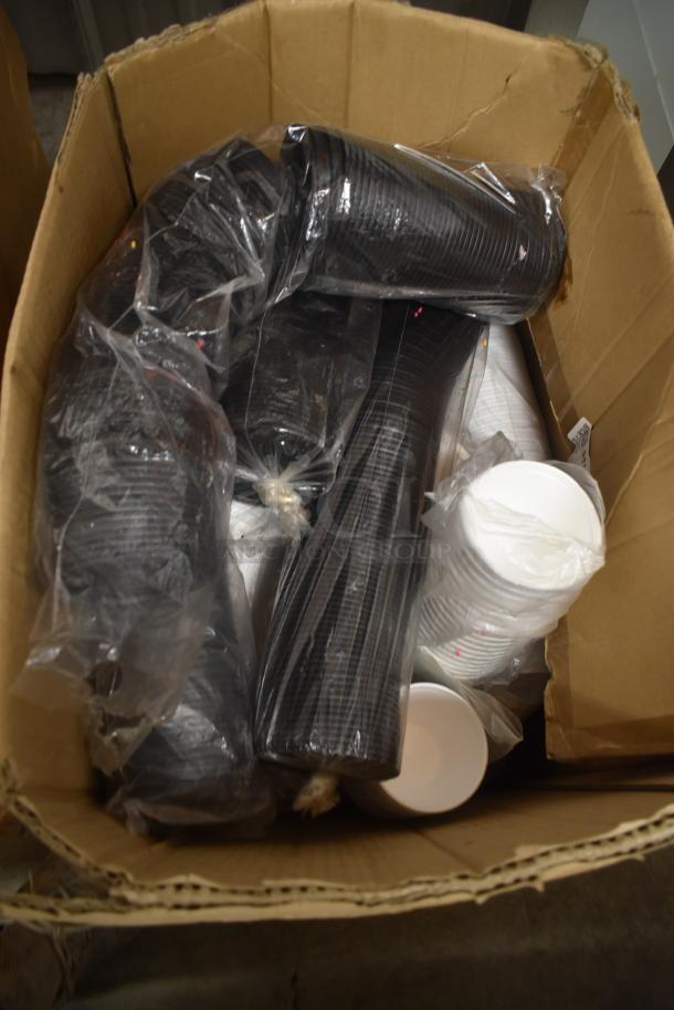 Box of disposable cups, black and white, in plastic sleeves. Condition appears new. Ideal for events or gatherings.