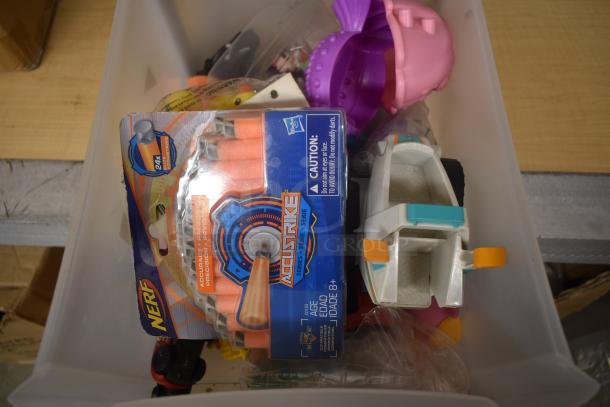 Box of assorted toys including a packaged Nerf Accustrike and toy boat. Nerf darts are visible, package is intact.