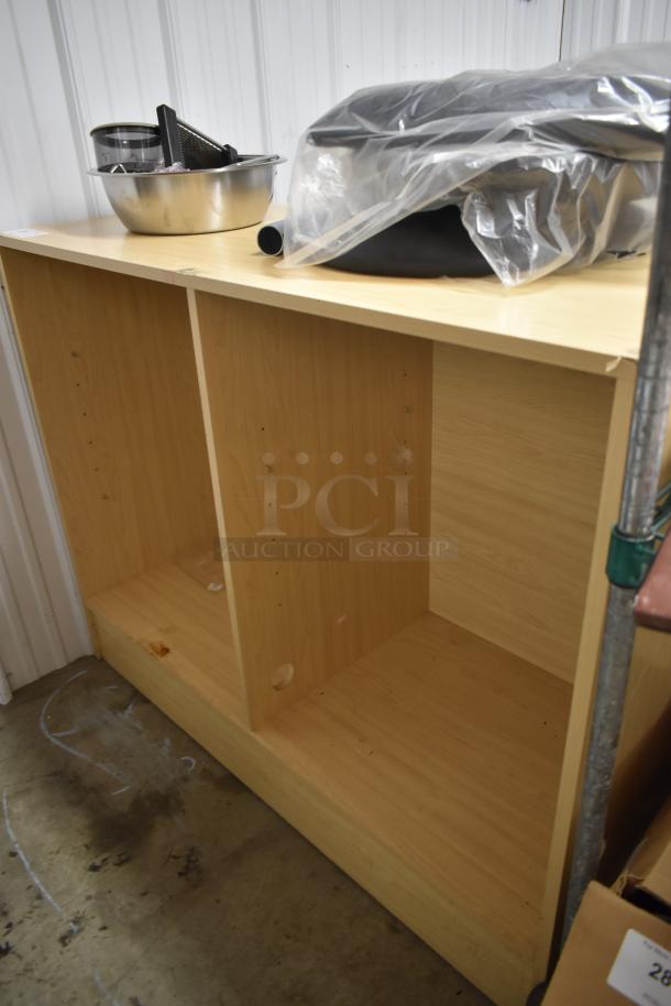 Wooden kitchen cabinet with two open shelves, light wood finish, some wear at the bottom corner. Metal bowl and plastic-wrapped item on top.