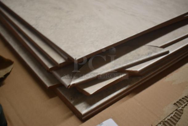 Stack of beige laminate flooring planks, showing edges and texture, in good condition on a cardboard surface.
